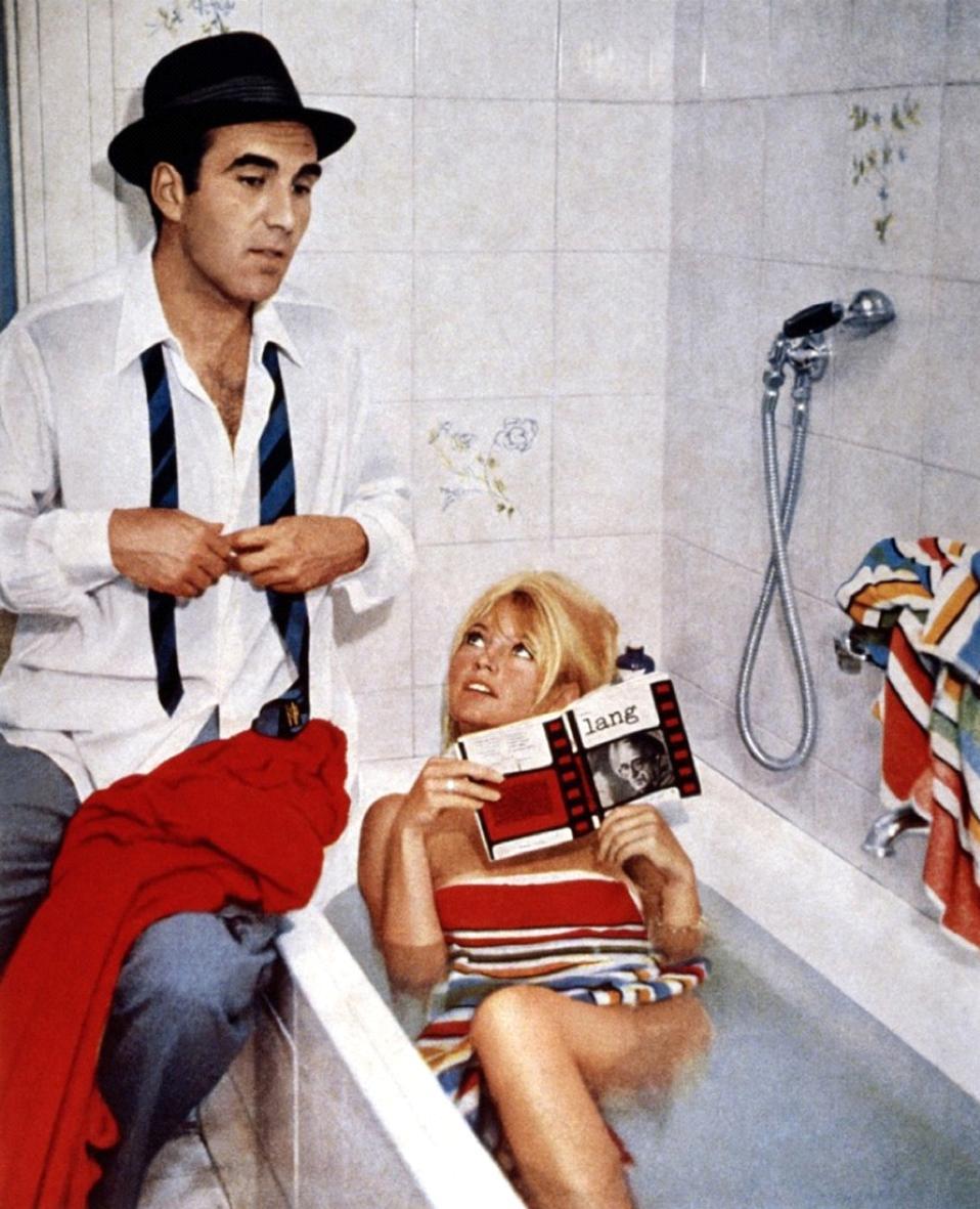 Still of Michel Piccoli sitting beside Brigitte Bardot as she bathes in Contempt.
